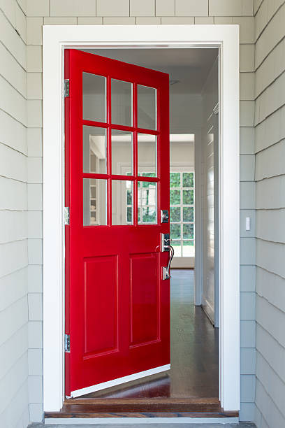 Front entrance to a residential home with a red solid wood door. The surrounding walls are covered with shingles.